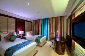 A hotel room with two beds, a desk, a chair, a TV, and a minibar.