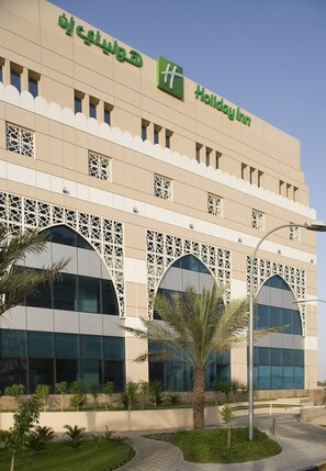 A Holiday Inn building with a modern facade, large windows, and a landscaped garden area with palm trees.