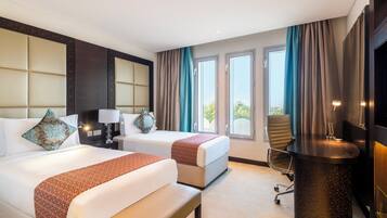 A hotel room with two beds, a desk, a chair, and a TV.