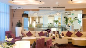 A modern lobby with seating areas, a staircase, and large windows.