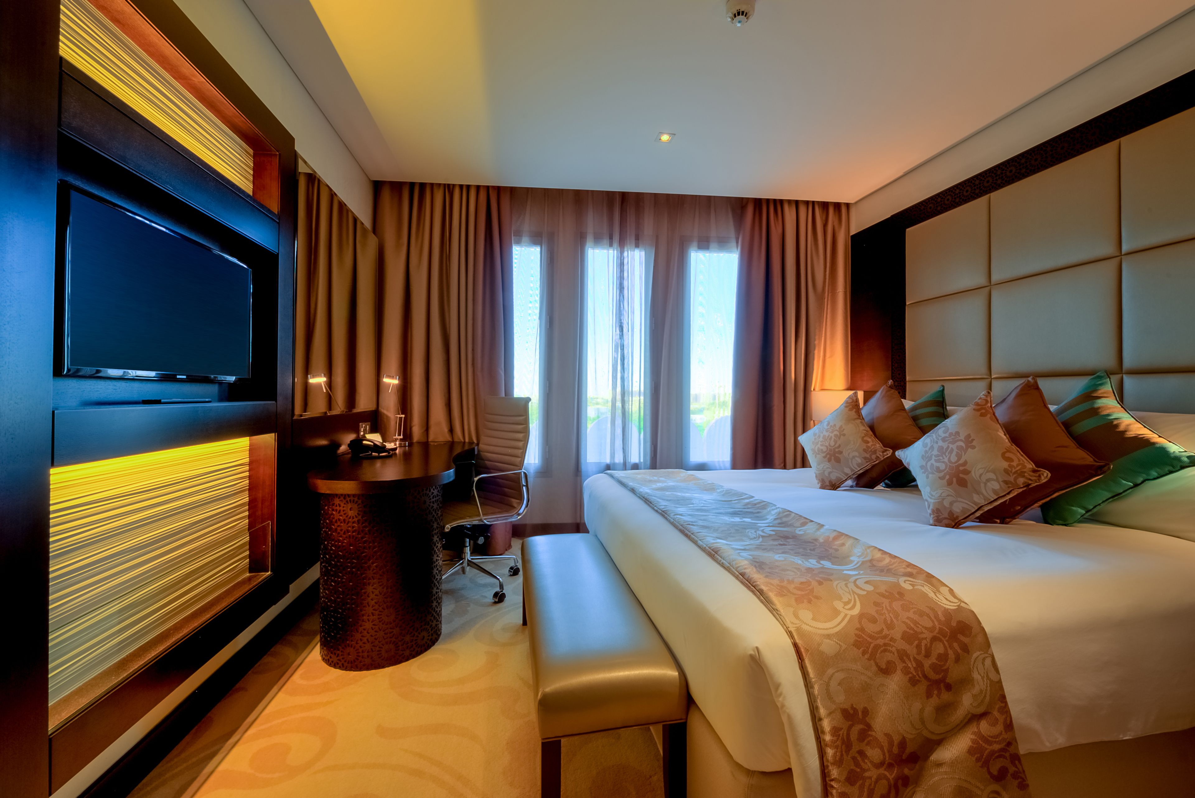 A hotel room with a large bed, a desk with a chair, a television, and a window with curtains.
