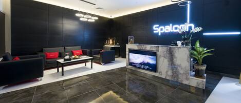 A modern reception area with a marble reception desk, a flat-screen TV, and a seating area with sofas and a coffee table.