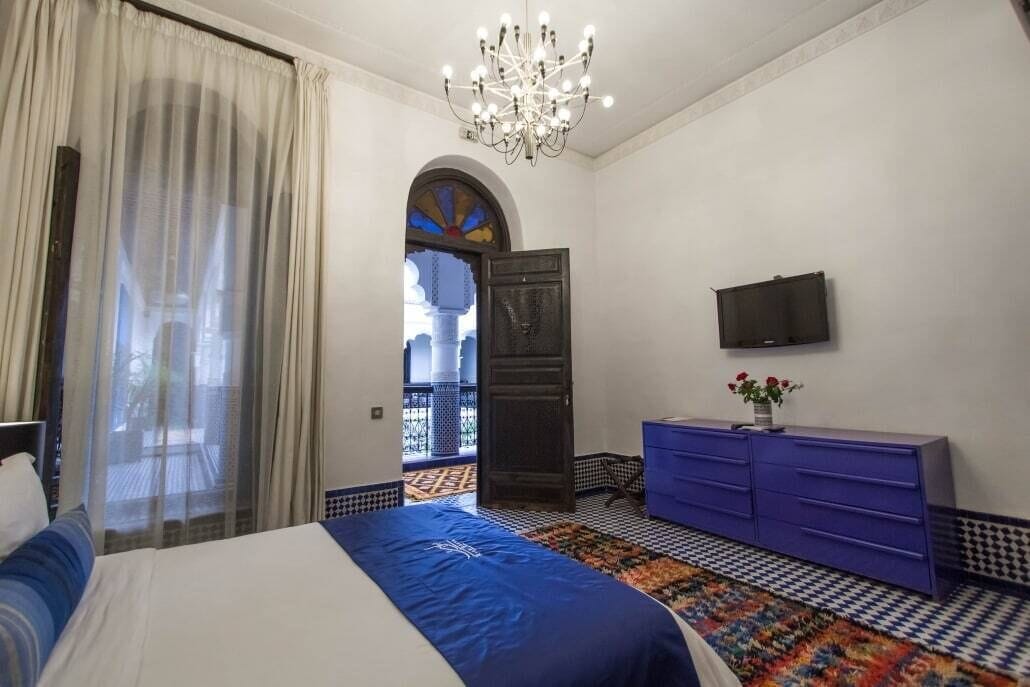 A bedroom with a bed, a dresser, a television, and a chandelier.