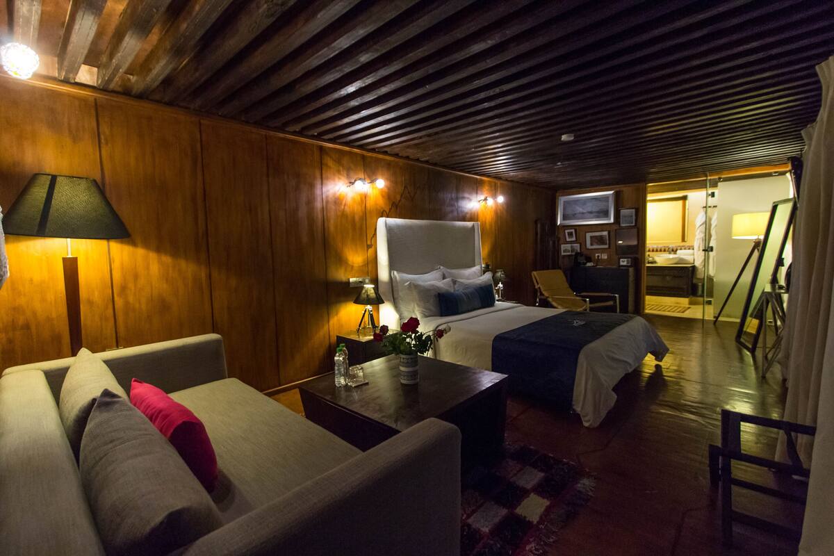 A hotel room with wooden paneling, a bed with a white headboard, a sofa, a coffee table, and a television.