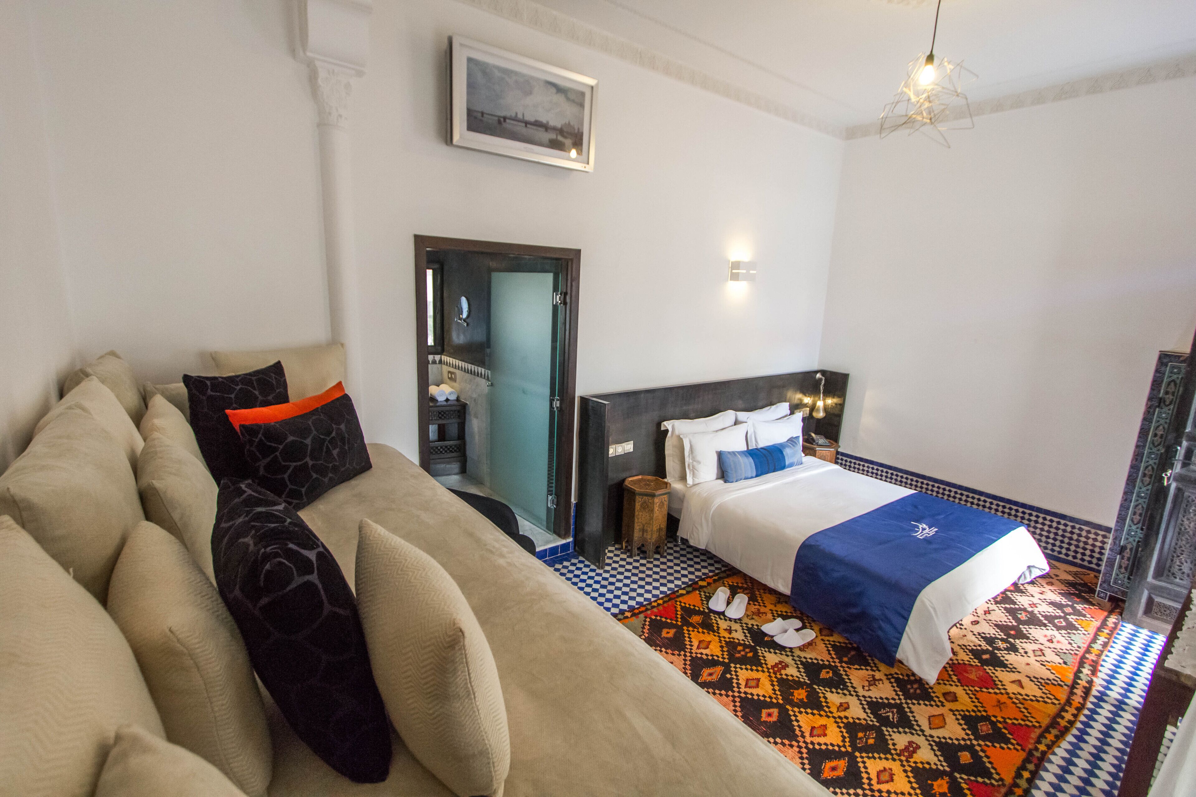 A hotel room with a bed, a sofa, a patterned rug, and a framed picture on the wall.