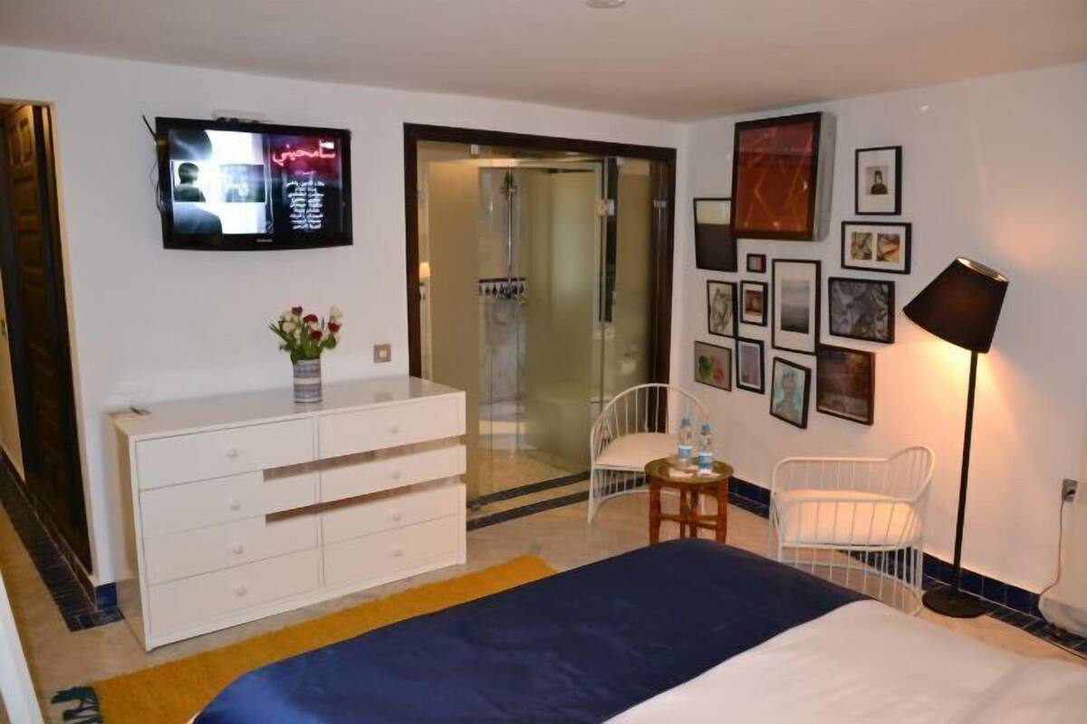 A hotel room with a bed, a TV, a dresser, a chair, a table, and a lamp.