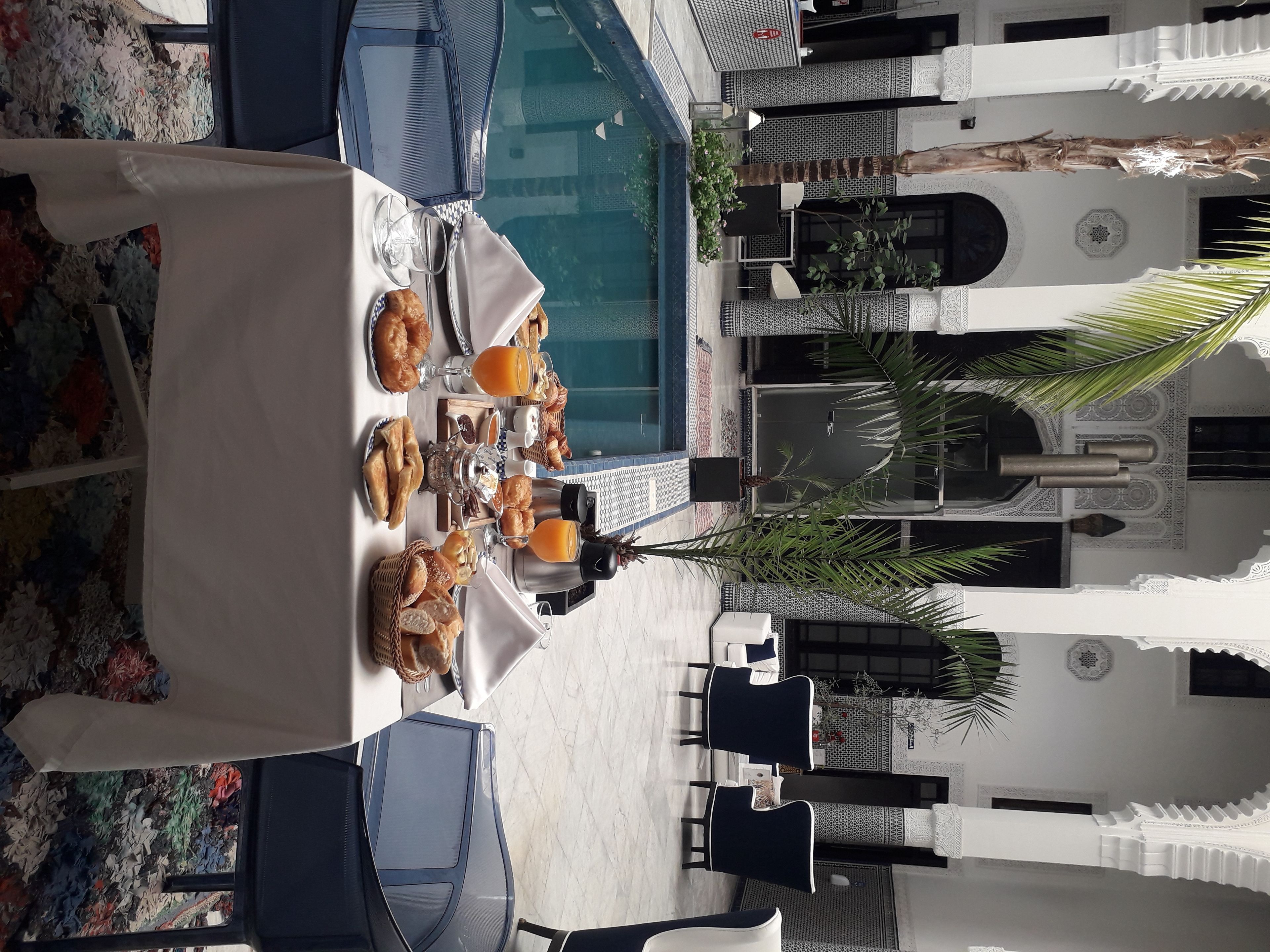 A dining area with a pool view, outdoor seating, and a buffet with pastries and drinks.