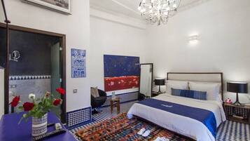 Una habitación de hotel con cama, una silla, una mesa con un jarrón de flores, una alfombra y un candelabro.