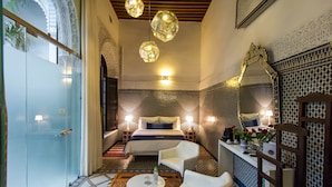 A hotel room with a bed, two chairs, a small table, a mirror, and patterned walls. - Riad Braya  (Fès)