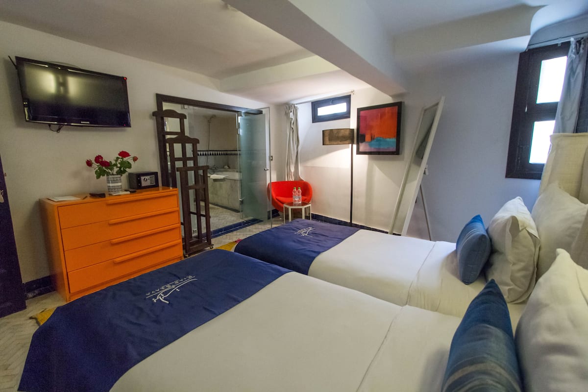 A hotel room with two beds, a TV, a dresser, and a bathroom visible through an open door.