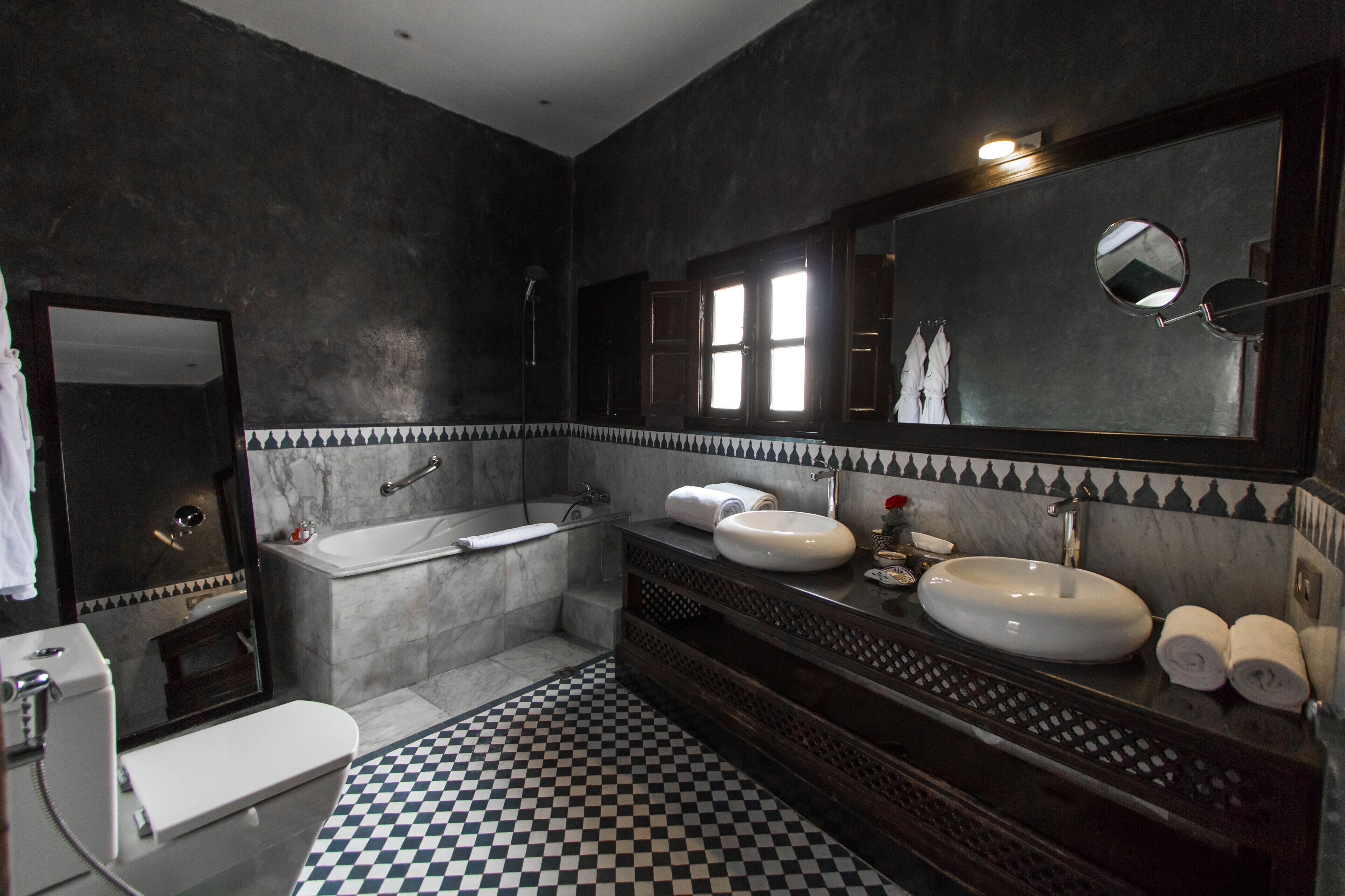 A bathroom with a checkered floor, a bathtub, two sinks, and a large mirror.