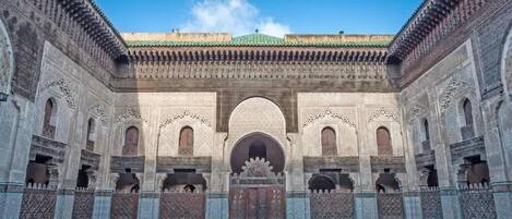 A courtyard with a central archway, surrounded by ornate walls and a tiled floor.