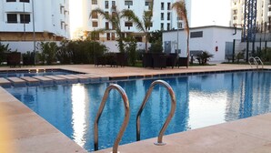 Una piscina con escalones de acceso, rodeada de un patio con mobiliario exterior y palmeras.