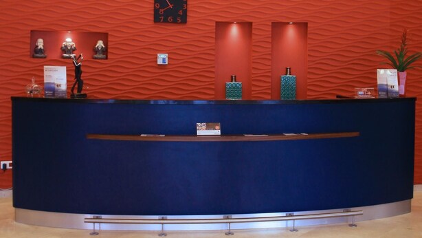 Zona de recepción con pared texturizada de color rojo, mostrador azul y un reloj.