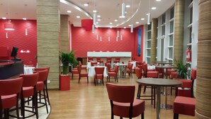 Un comedor moderno con sillas y mesas rojas, un mostrador de recepción y un ventanal con vistas.