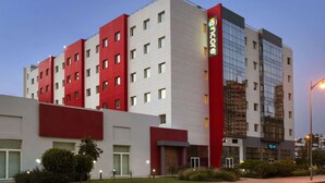 Un hotel de varios pisos con fachada roja y blanca, grandes ventanales y una entrada visible.
