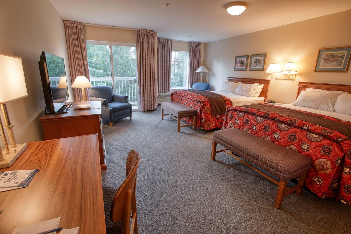 A hotel room with a bed, two chairs, a desk, a bench, and a television.
