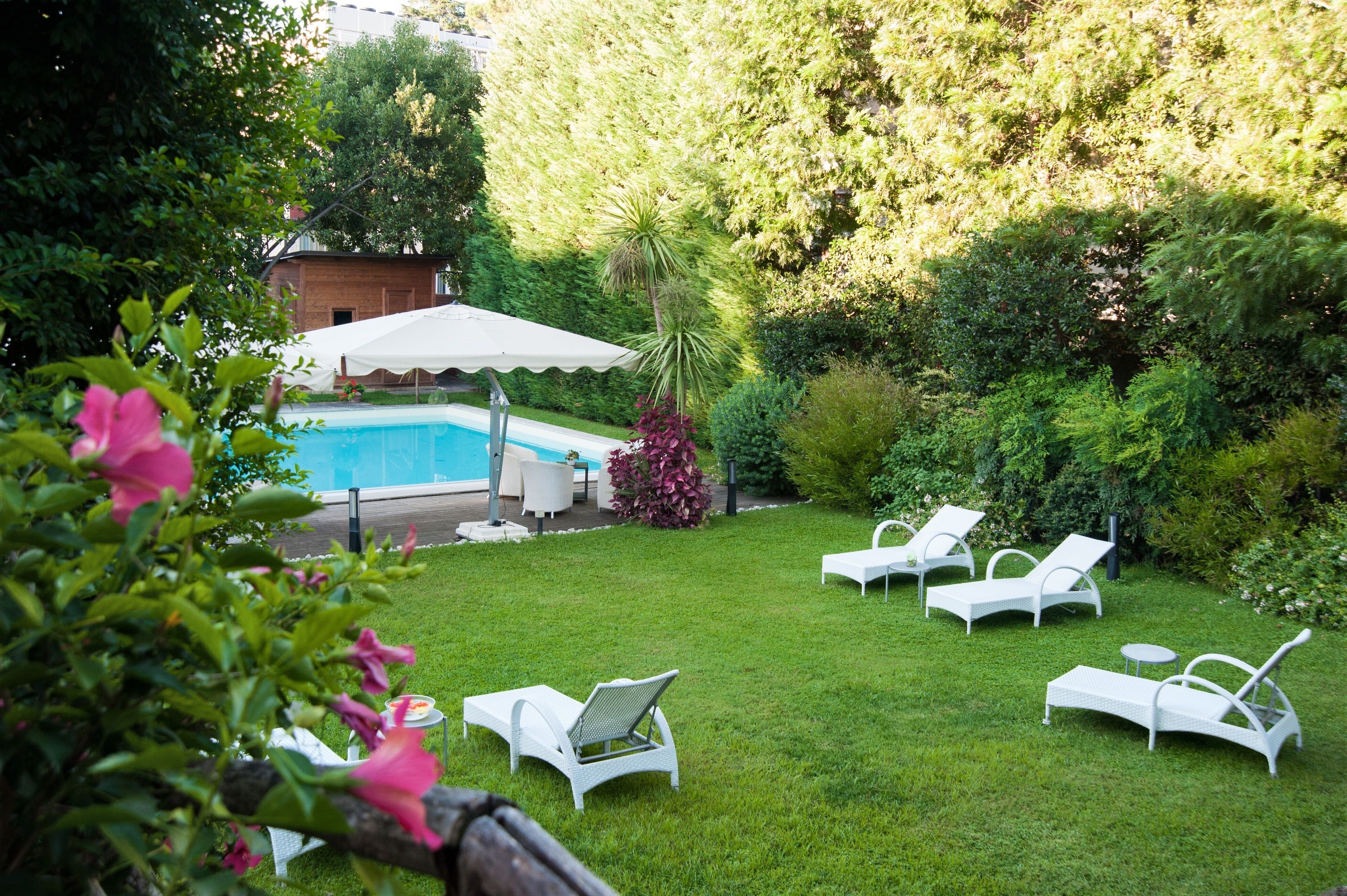 A backyard with a swimming pool, white lounge chairs, and a covered seating area.