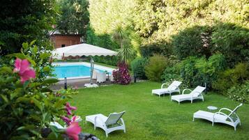 A backyard with a swimming pool, white lounge chairs, and a covered seating area.