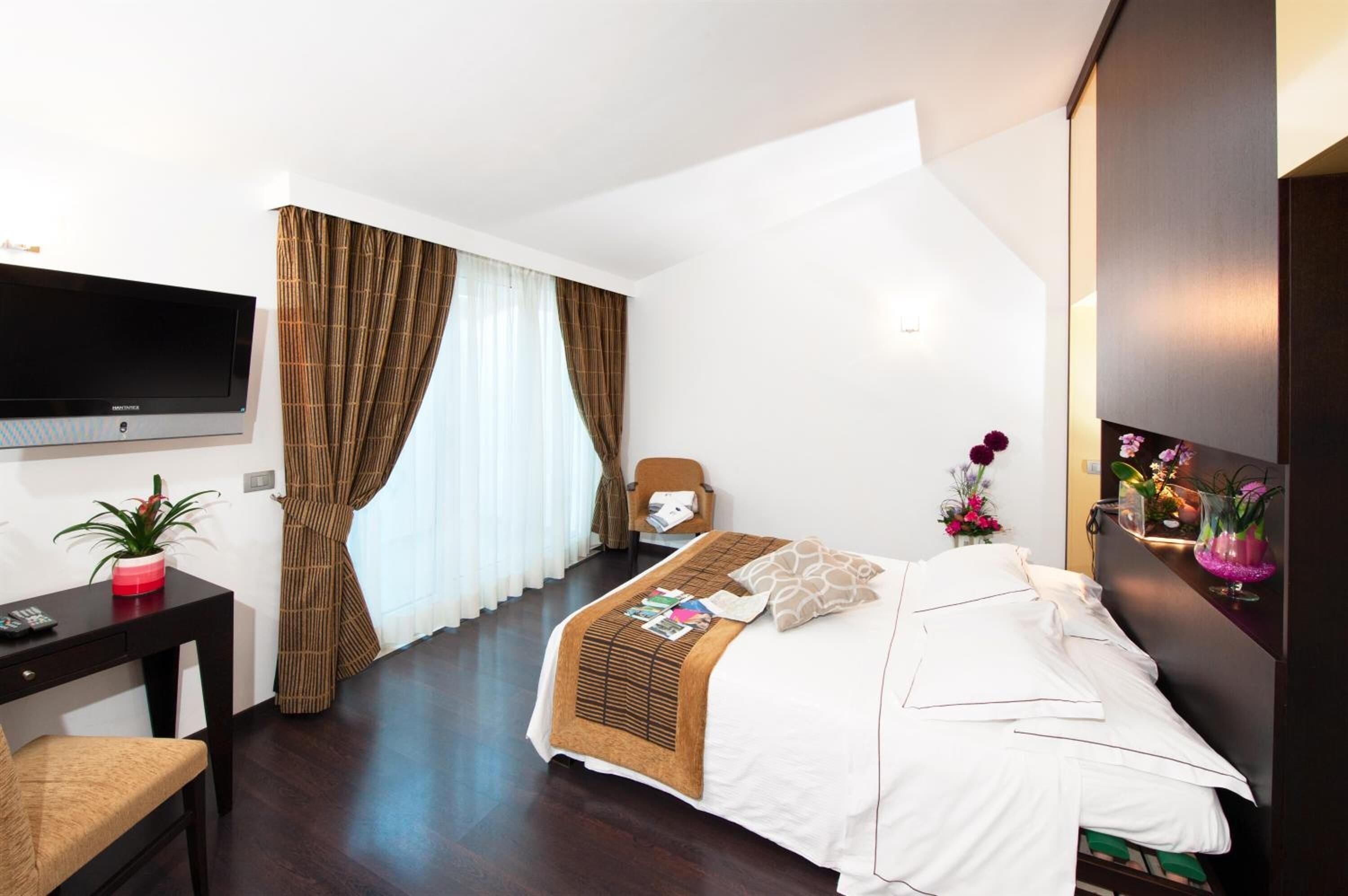 A hotel room with a bed, a desk, a chair, a TV, and a wall-mounted artwork.