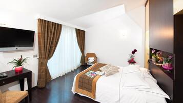 A hotel room with a bed, a desk, a chair, a TV, and a wall-mounted artwork.