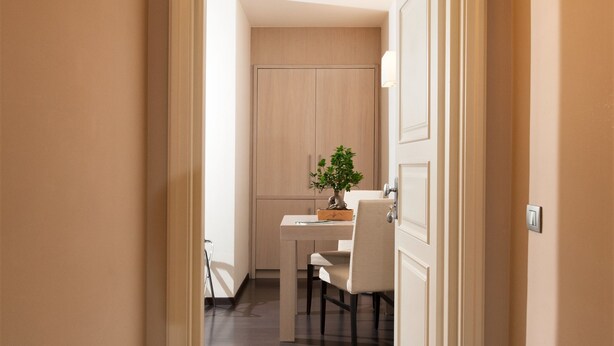 Un pasillo que conduce a un comedor con una mesa, sillas, una planta en maceta y una puerta.