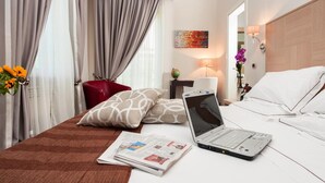 Habitación de hotel con cama, computadora portátil, periódico, lámpara y un florero con flores.