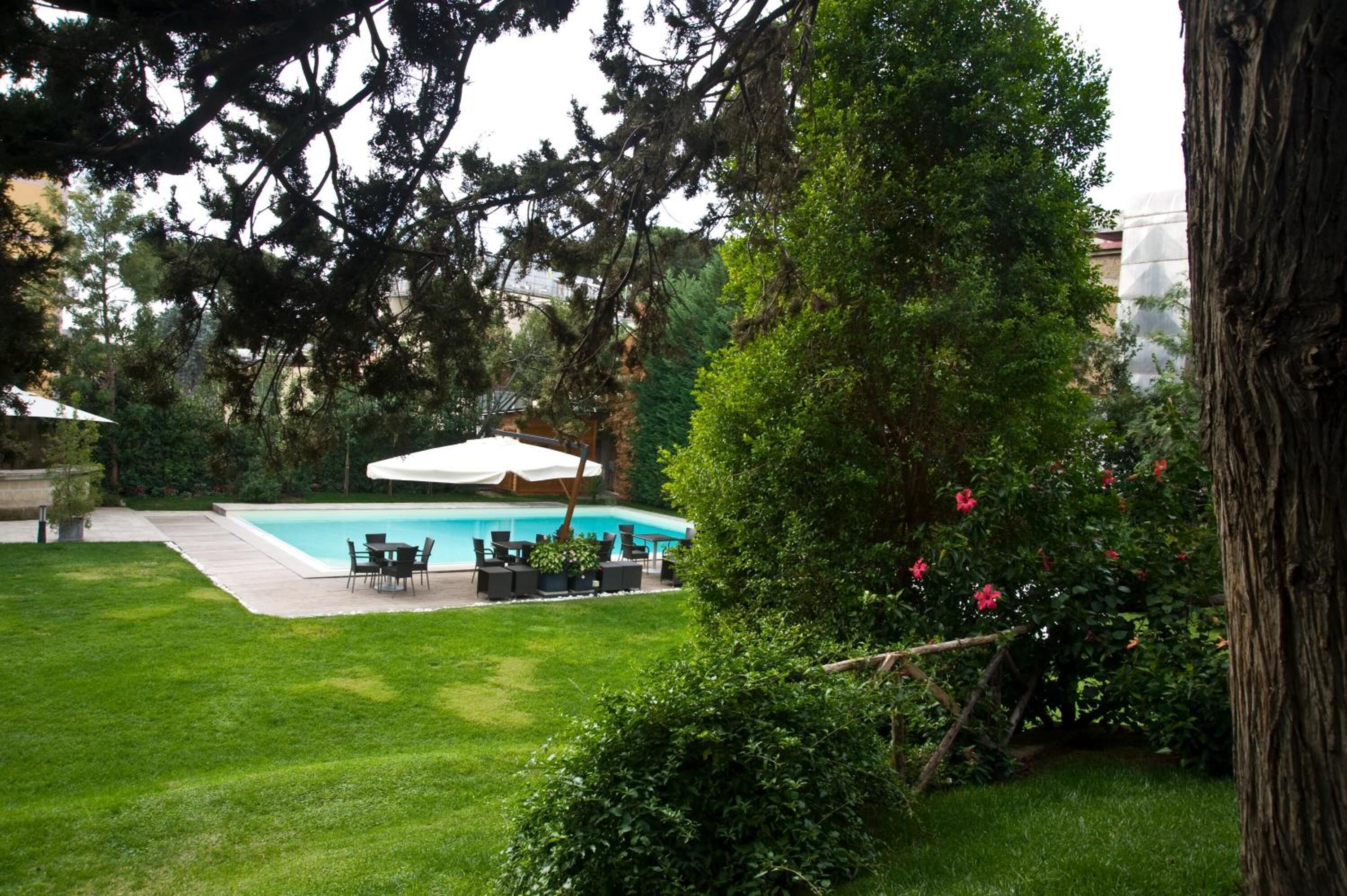 A swimming pool with a white umbrella, surrounded by a well-maintained lawn and various plants.