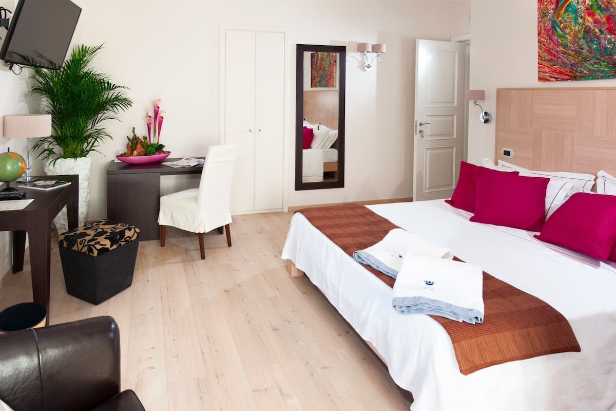 A hotel room with a bed, desk, chair, and a large mirror.