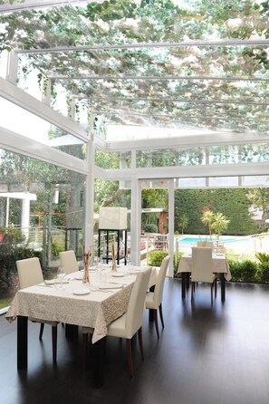 Comedor con una mesa dispuesta para seis personas, sillas alrededor y techo de cristal que deja entrar luz natural.