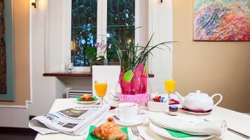 Ein Frühstückstisch mit Zeitung, Croissant, Kaffeetasse, Teekanne und Orangensaftgläsern.