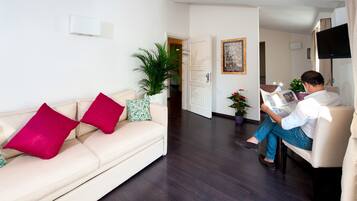 A living room with a sofa, a coffee table, a potted plant, and a person reading a book.