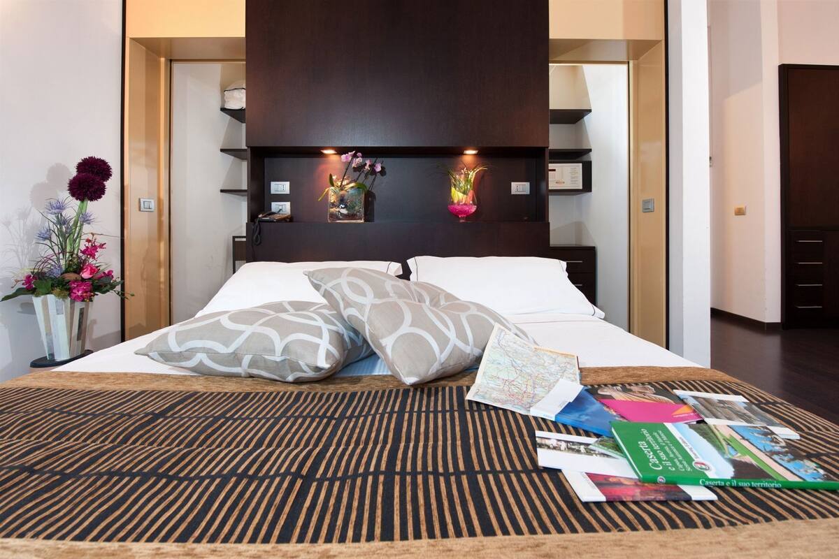 A modern hotel room with a bed, a patterned rug, a nightstand with a vase of flowers, and a map on the bed.