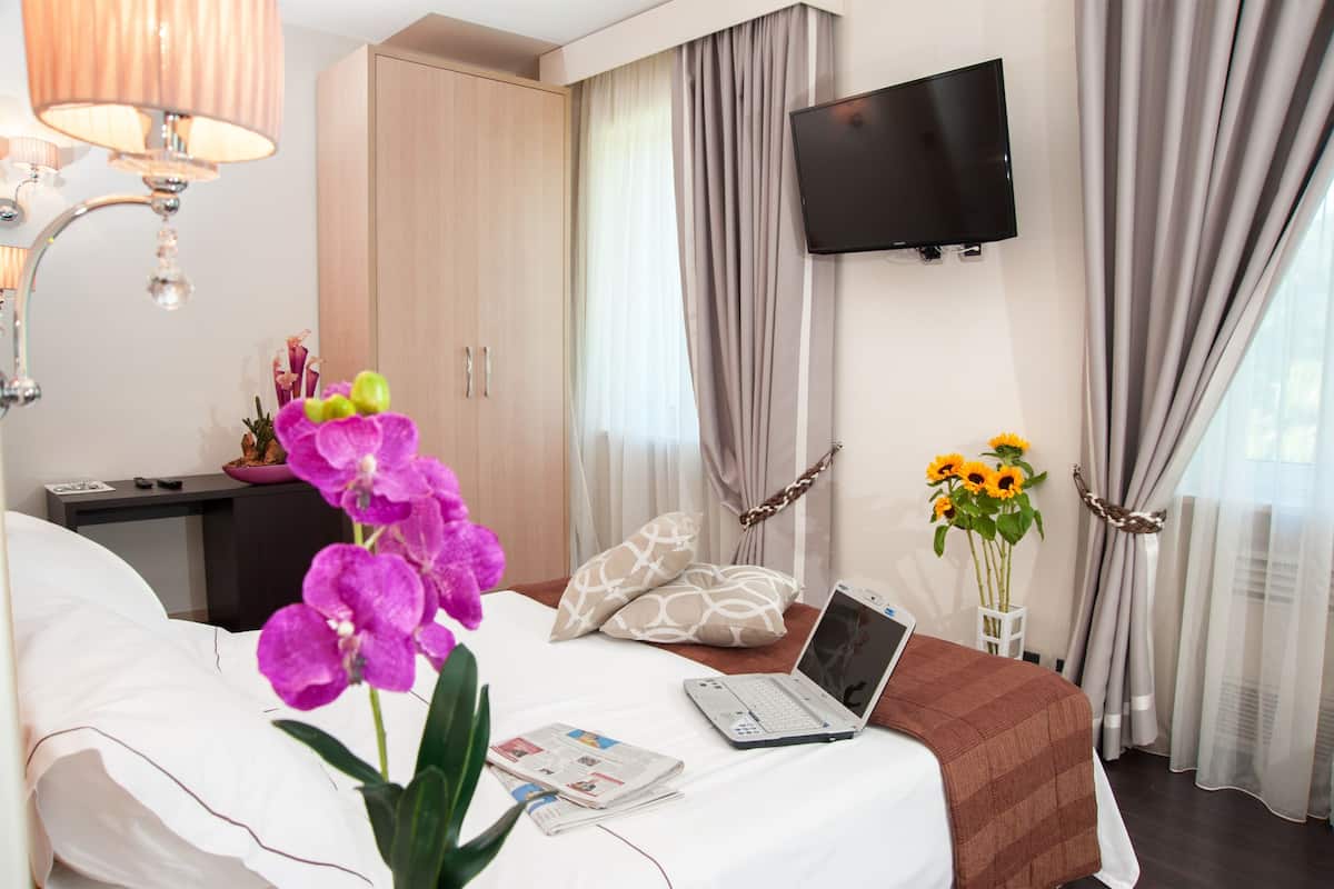 A hotel room with a bed, a desk with a laptop, a TV, and a vase with sunflowers.
