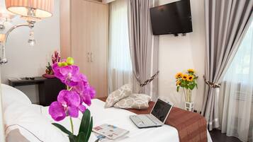 A hotel room with a bed, a desk with a laptop, a TV, and a vase with sunflowers.
