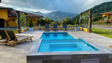 Relax by the serene pool surrounded by lush green hills and a patio with lounge chairs.