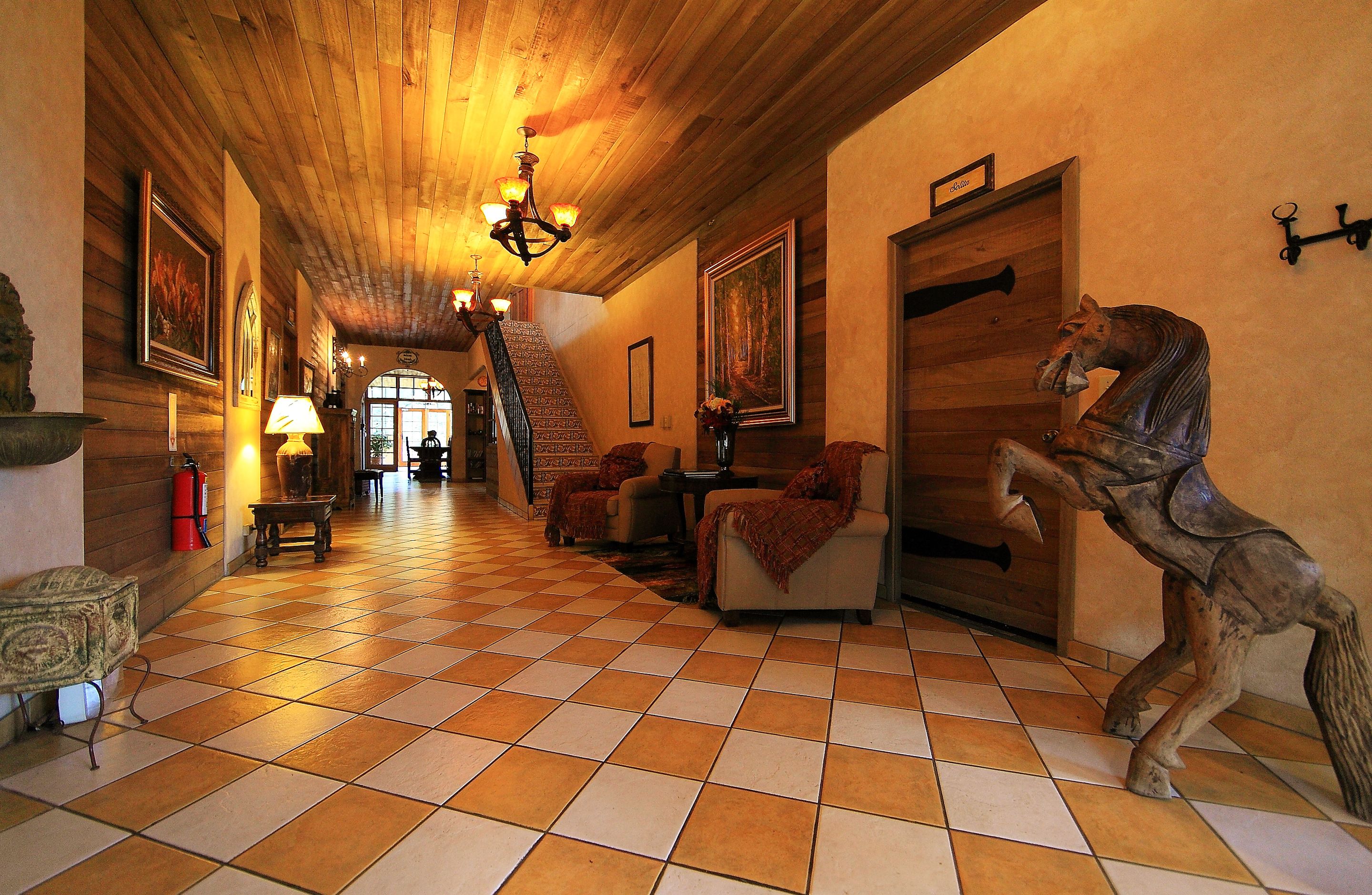 A spacious hallway with a checkered floor, a chandelier, and a horse statue.