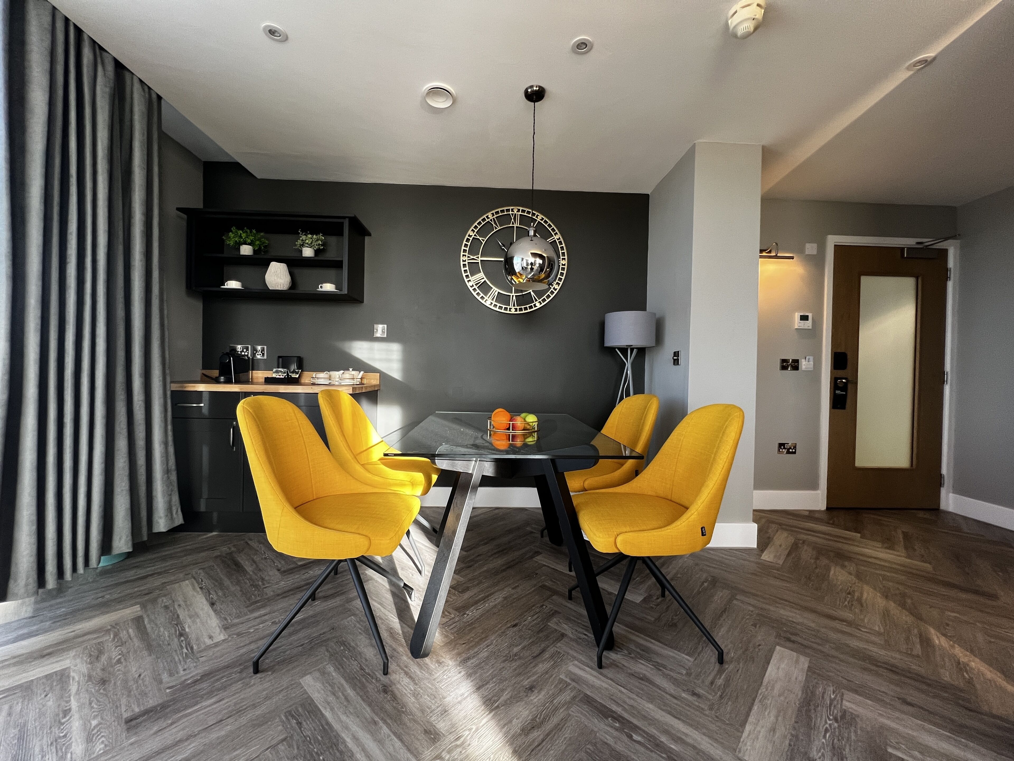 Un comedor moderno con una mesa redonda, dos sillas amarillas y un reloj decorativo en la pared.
