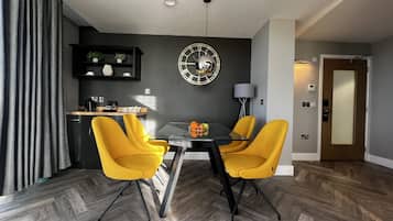 A modern dining area with a round table, two yellow chairs, and a decorative wall clock.