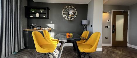 A modern dining area with a round table, two yellow chairs, and a decorative wall clock.