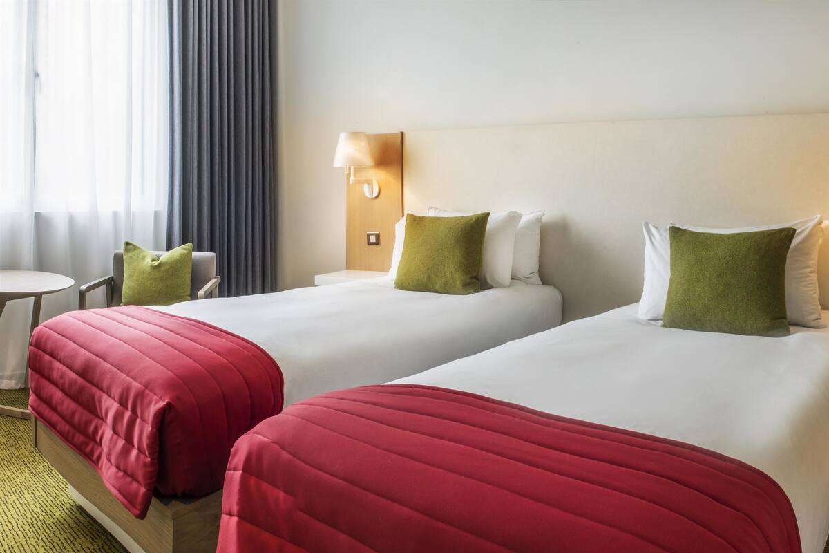 Hotellihuoneessa on kaksi sänkyä, joissa on punaiset päiväpeitteet ja vihreät tyynyt. Lisäksi huoneessa on pieni pöytä ja tuoli. Sänkyjen molemmilla puolilla on seinään kiinnitetyt lamput.
