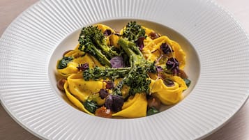 A white plate with a textured edge, containing a pasta dish with broccoli and purple leaves, possibly microgreens, on a wooden table.