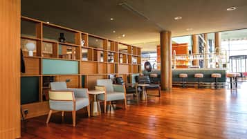 Un'ampia area lounge con scaffali in legno, sedute confortevoli e un bar sullo sfondo.