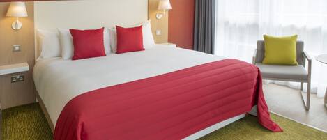 A hotel room with a large bed, two bedside lamps, a chair, and a window with curtains.