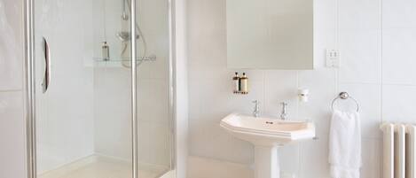 A modern bathroom with a glass-enclosed shower, a pedestal sink, and a large mirror.