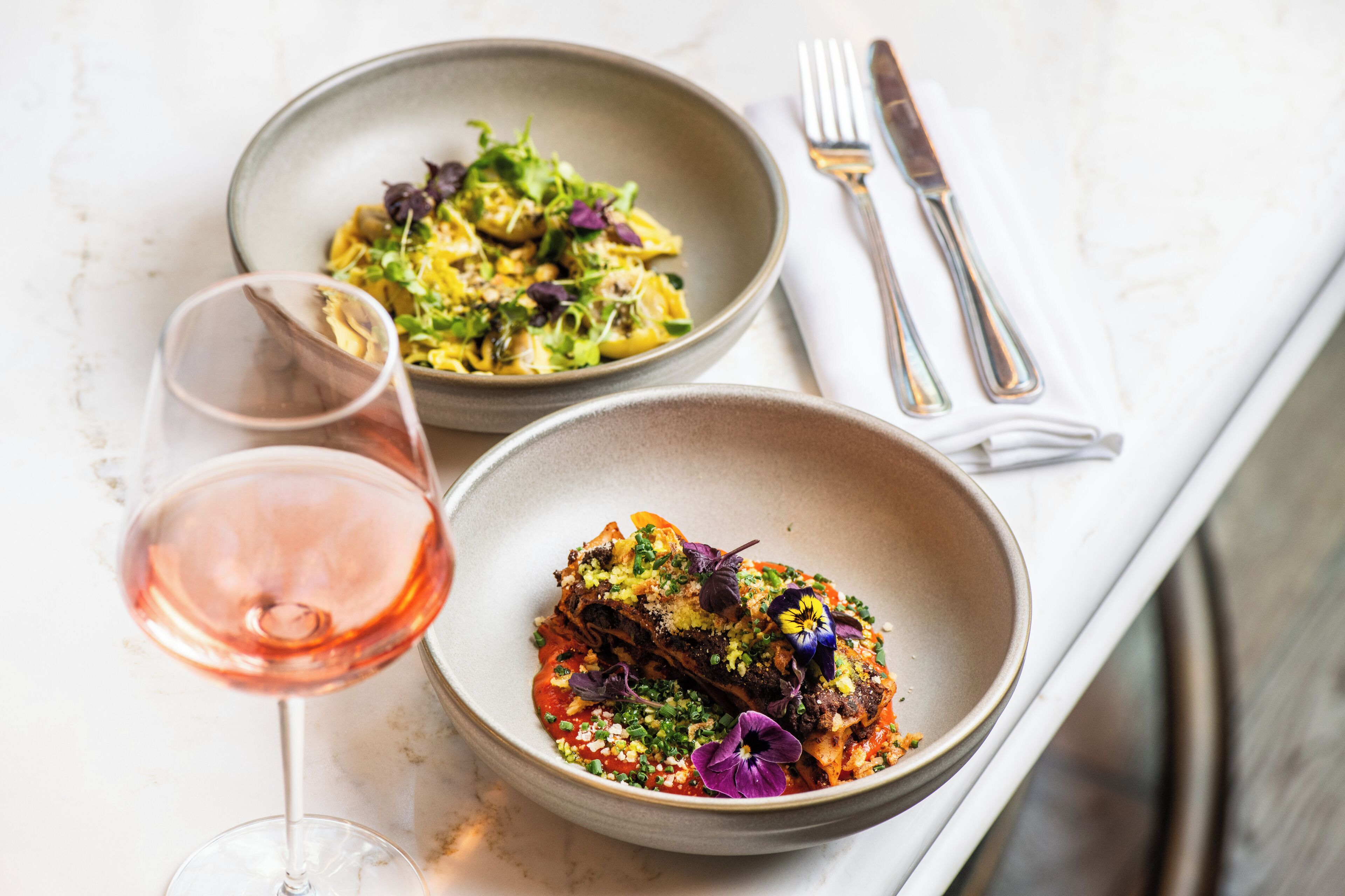 Two plates of food on a table with a wine glass.