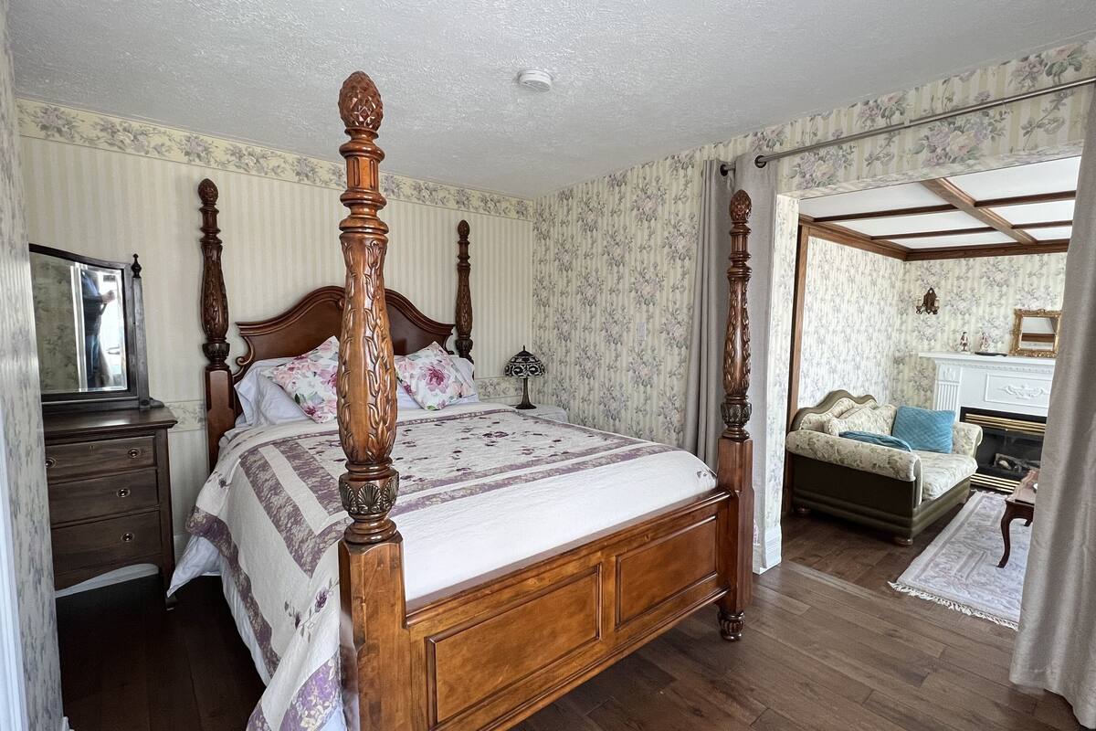 A four-poster bed with a floral bedspread, a wooden nightstand with a lamp, and a dresser with a mirror.