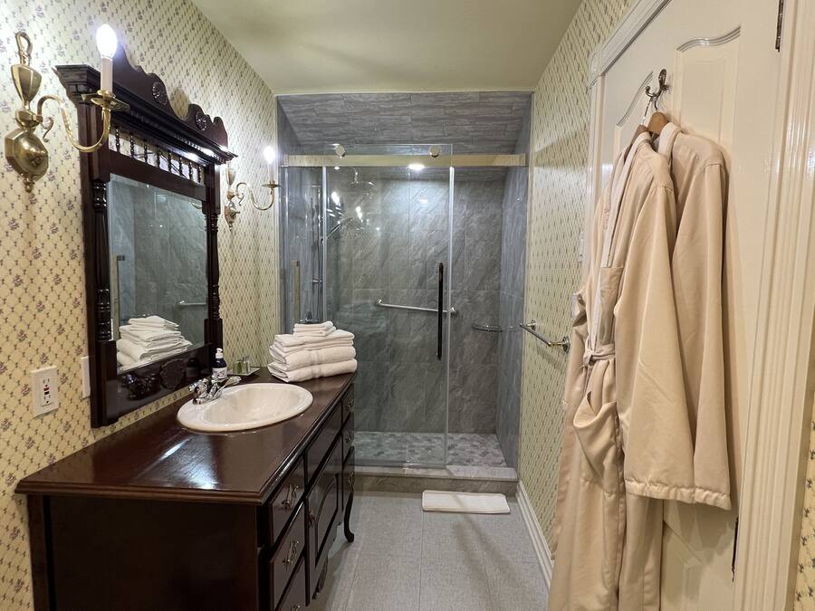 A bathroom with a vanity, a large mirror, a shower with a glass door, and a towel rack with towels.