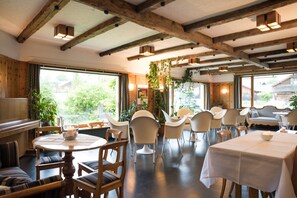 Enjoy meals in a spacious dining area with round tables, modern chairs, and large windows offering views of the surrounding greenery.