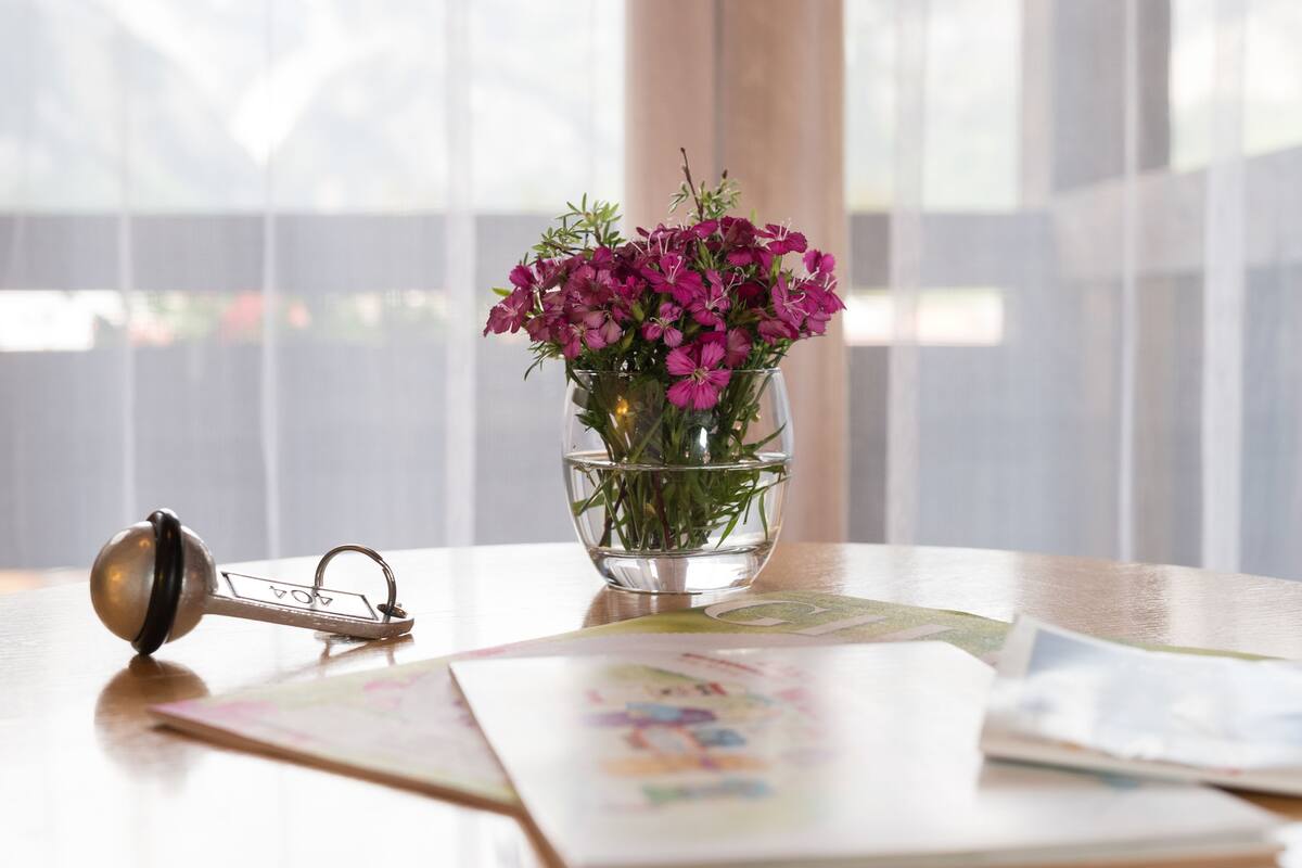 A clear glass vase with pink flowers on a wooden table, a keychain, and a children's book.